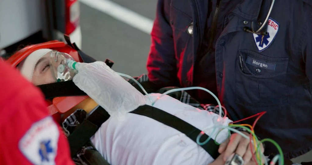 Patient on an ambulance stretcher with an oxygen mask and head immobilization, symbolizing a severe spinal cord injury and its potential for permanent disabilities.