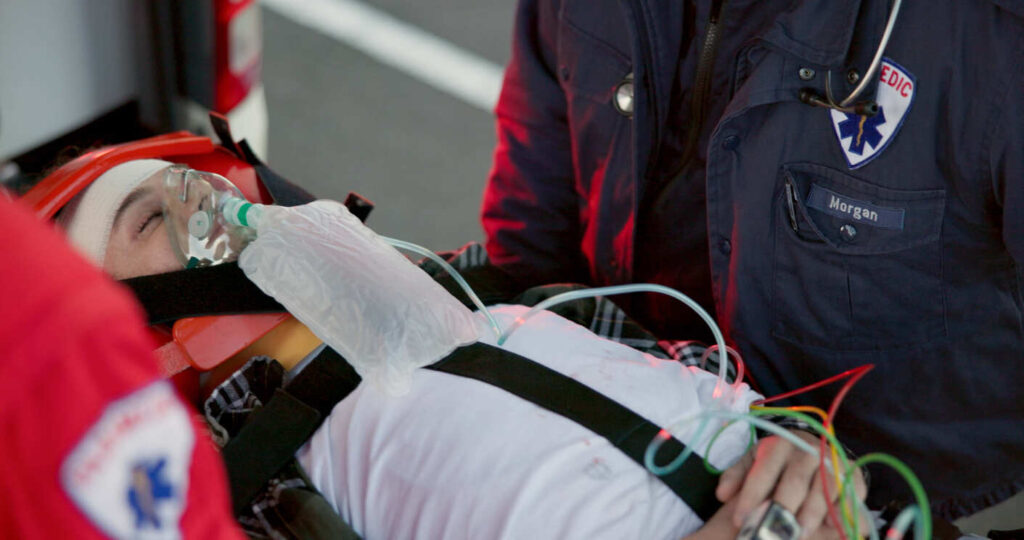 Patient on an ambulance stretcher with an oxygen mask and head immobilization, symbolizing a severe spinal cord injury and its potential for permanent disabilities.