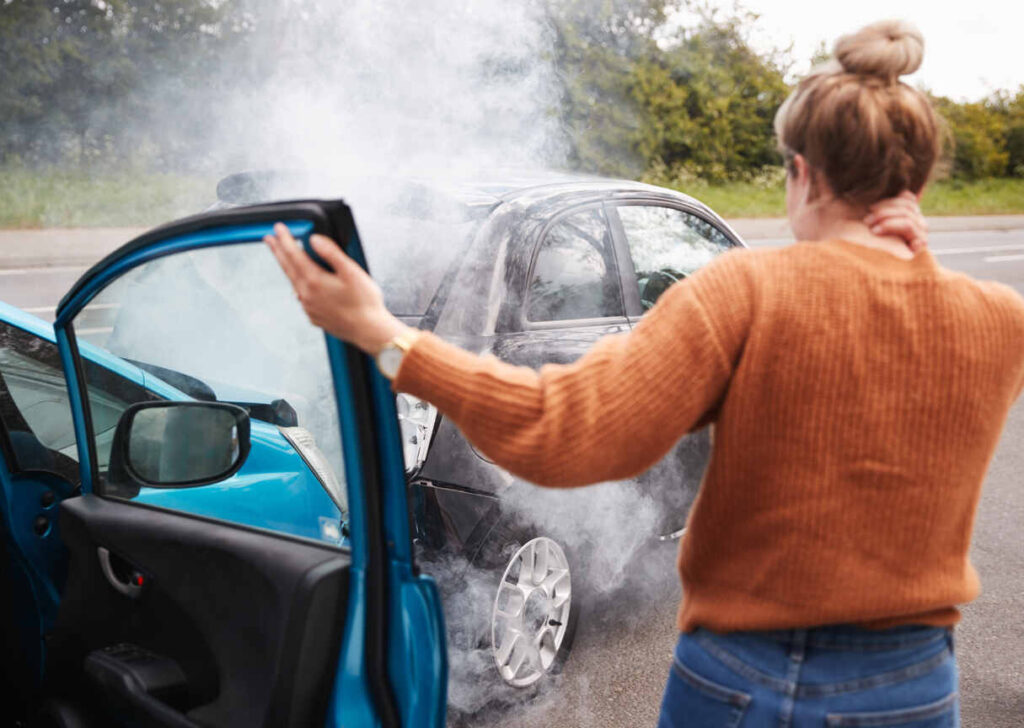 Woman holding her neck in pain next to two cars involved in a smoky collision, emphasizing the immediate need for medical attention after a car accident in NC.