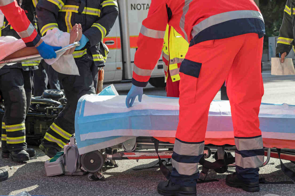 Emergency responders carefully moving an injured person onto a stretcher at an accident scene, symbolizing severe injuries from a motorcycle crash that may necessitate orthopedic surgery.