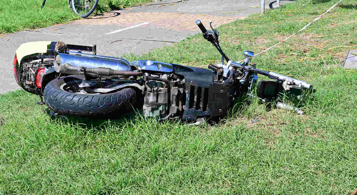 A motorcycle lies on its side in a grassy area next to a paved road, depicting the aftermath of a collision.