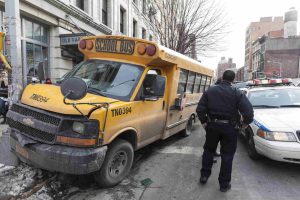 A school bus involved in a collision with a truck, with a police officer on the scene in a busy urban area.