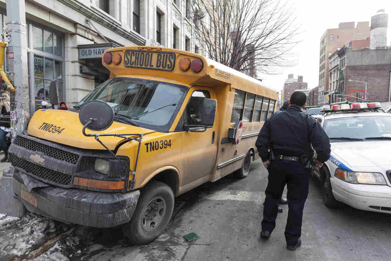 A school bus involved in a collision with a truck, with a police officer on the scene in a busy urban area.