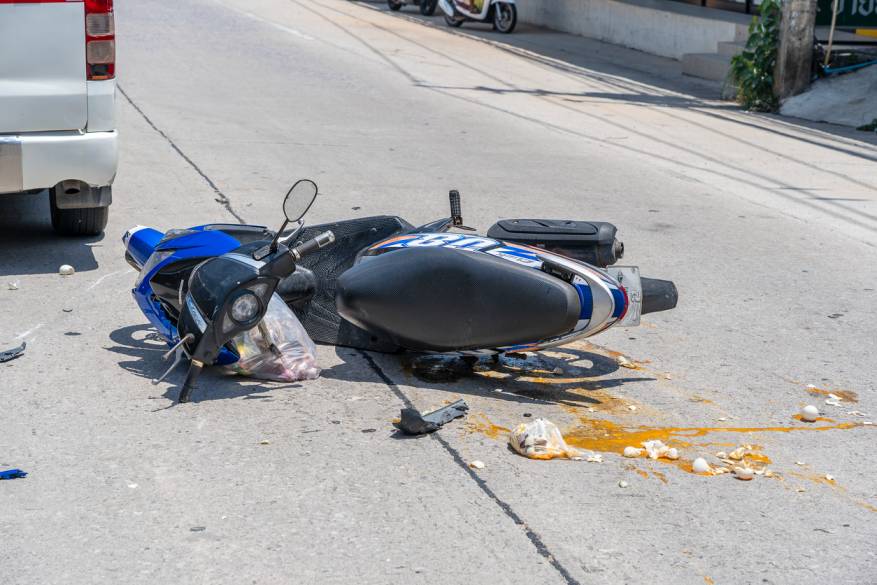Motorcycle accident on the street with a damaged scooter and spilled contents on the road, indicating a crash scene.