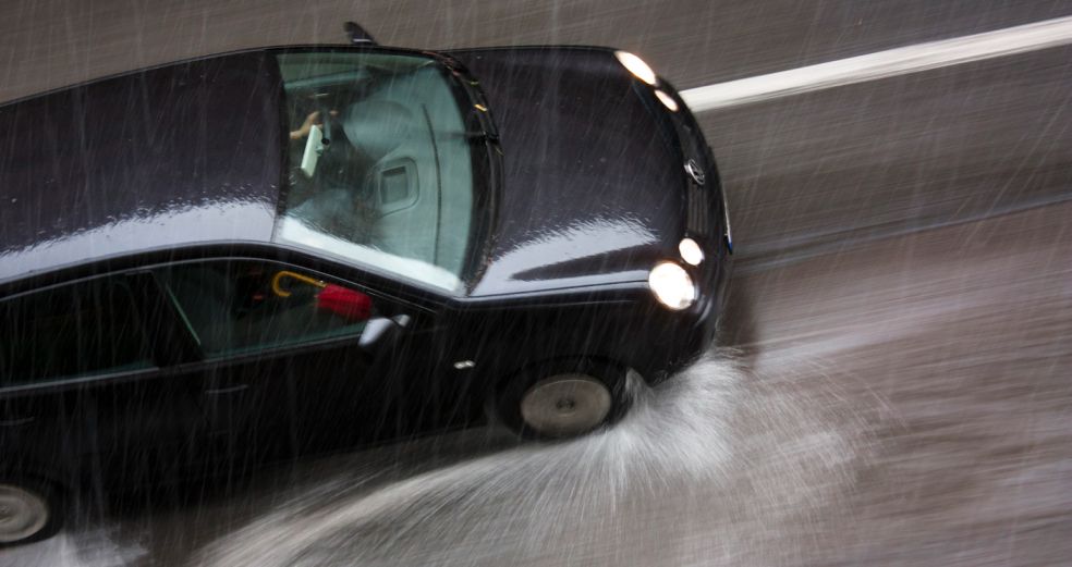 Car driving through heavy rain, losing traction on wet road, potentially causing a rain-related accident.