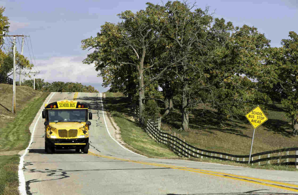School bus on rural road with 'School Bus Stop Ahead' sign, highlighting the need for caution in areas with children, relevant for news on fatal collision in Pender County involving students.